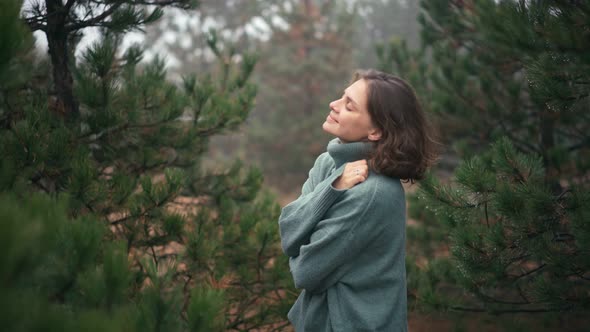 A Young Woman Wrapping Herself in a Cozy Warm Sweater While in the Misty Forest