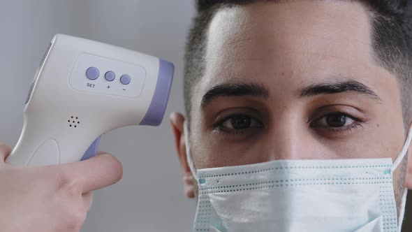 Closeup View Infrared Scanner on Male Customer's Forehead Arabian Man in Protective Medical Mask