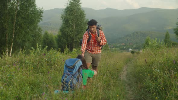 Caring African Male Hiker Helping Asian Woman Traveler to Stand Up Off Ground on Trek