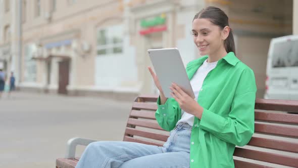 Hispanic Woman Celebrating Online Win on Tablet While Sitting Outdoor on Bench