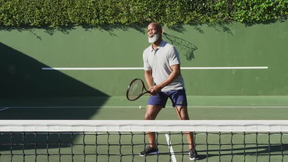 African american senior man playing tennis on the tennis court on a bright sunny day