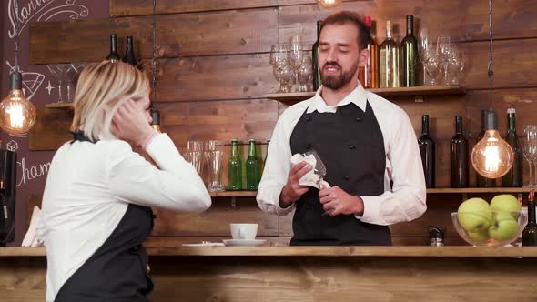 Bartender Cleans a Glass and Listens Very Concentrated To His Female Coworker