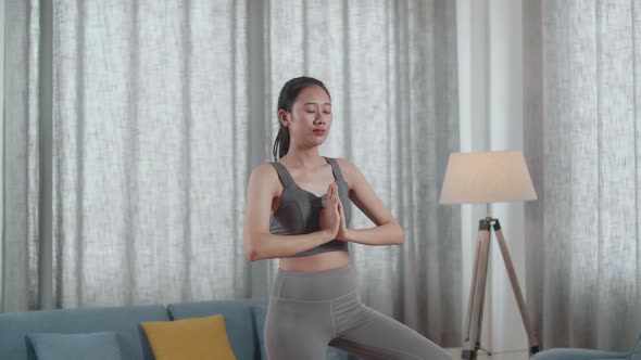 Young Asian Athletic Female In Sports Clothes Doing Yoga In Tree Pose On The Mat At Home