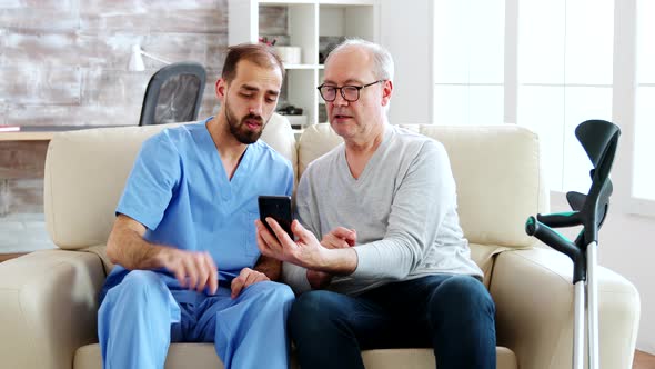 Male Nurse Helps a Retired Old Man To Use a Smartphone