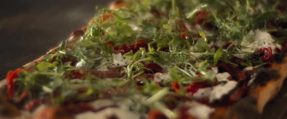 Close up of burrata al taglio pizza with cheese, re peppers and fresh green herbs.