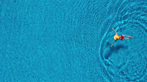 View From the Top As a Woman in a Red Swimsuit and a Big Yellow Hat Swims in the Pool