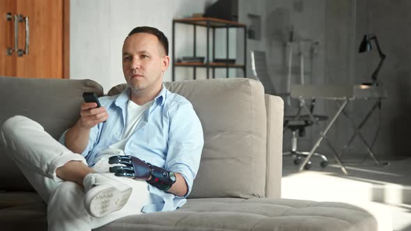 Relaxed man with high tech bio hand prothesis takes remote controller