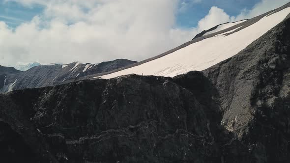 Two People Hiking Along Rocky Trail Snowy Path in Sunny Day Near the Big Cliff