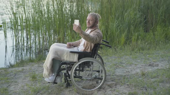 Side View of Positive Disabled Man on Wheelchair Talking Via Video Chat at Selfie Camera on