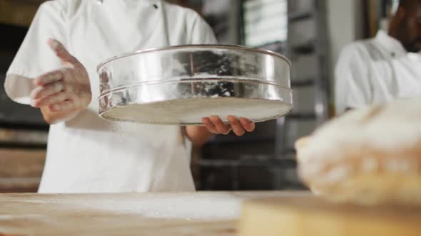 Animation of midsection of asian female baker sieving flour on board