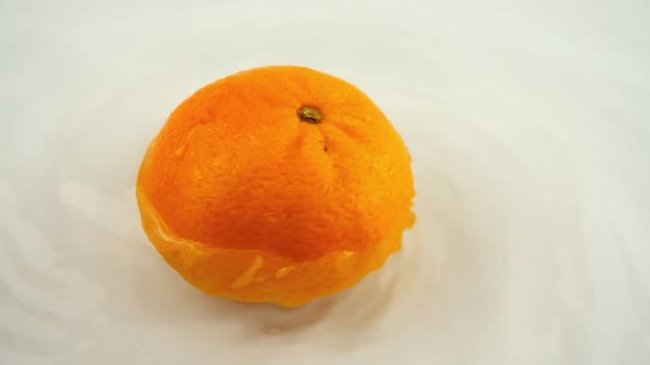 Rotating ripe orange in water on a white background. Slow motion.