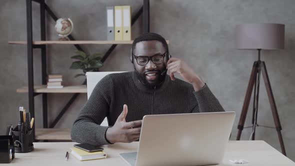 African American Male in Headset Consult Online Using Laptop \ Black Man in Headphones Leads an