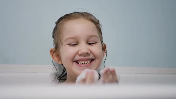 Cute Preschooler Girl Takes a Bath with Foam Plays Laughs Blowing Off the Foam