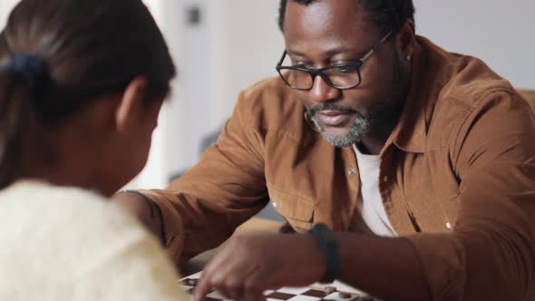 Cheerful African father and daughter playing checkers