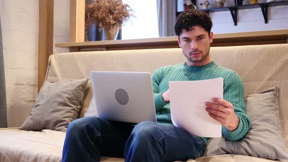 Paperwork on Laptop and Documents By Man Sitting on Couch at Home