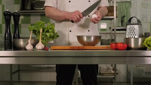Chef Breaks a Chicken Egg Over a Plate in a Professional Kitchen in a Restaurant