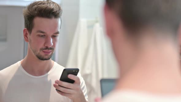 Young Man Using Smartphone in Mirror