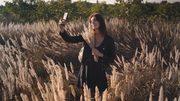 Attractive Fun Stylish Redhead Woman in the Field at Sunset Making a Selfie with a Bouquet of