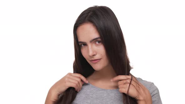 Portrait of Cute Caucasian Woman Posing at Camera with Playful Look Touching Her Long Dark Hair