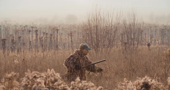 Hunter in hunting equipment with a rifle in his hand sneaks through the bush in the field