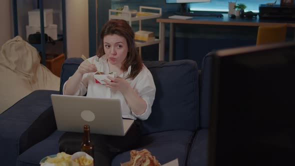 Young Woman Using Laptop on Sofa While Eating Asian Food