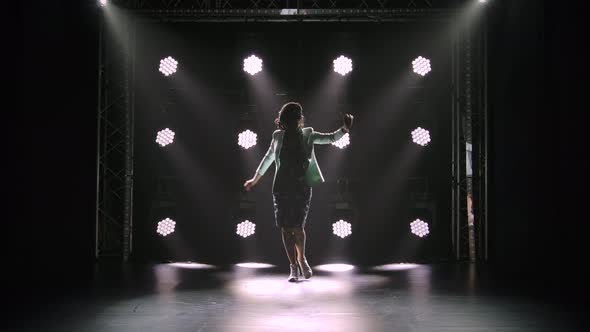 An Attractive Middle Aged Brunette Walks in a Dark Studio Against the Backdrop of Neon Lights. A