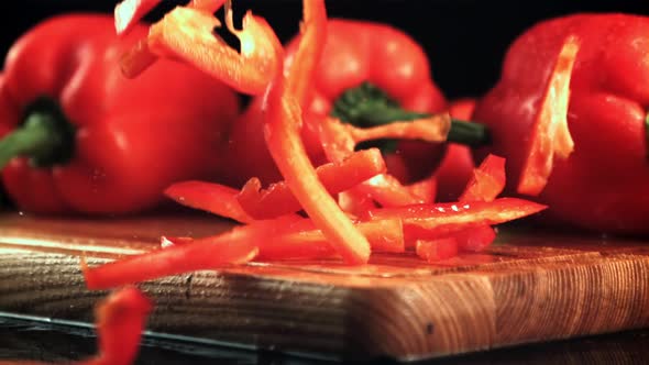 Pieces of Red Sweet Pepper Fall on a Wooden Cutting Board