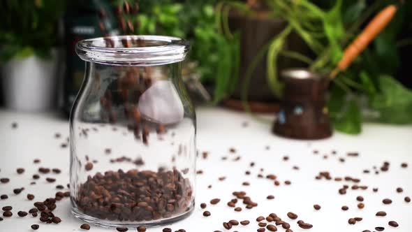 Slow Motion Empty Transparent Jar Filled with Coffee Beans on White Table with Coffee Beans Lay on