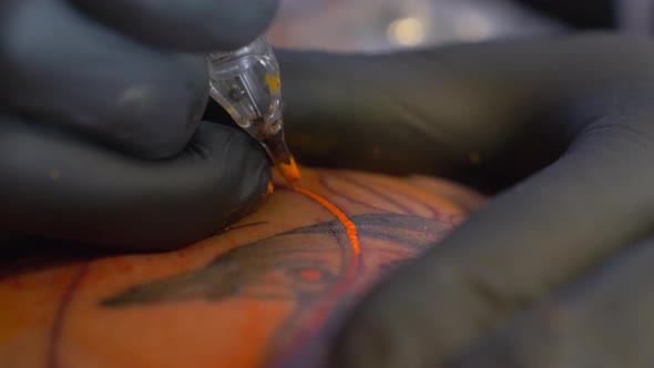 A Tattoo Artist Putting Orange Color On The Design He Draw On His Client's Arm - Close Up Shot