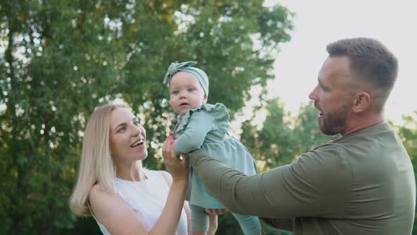 Happy Couple Playing with Baby Daughter on Lawn in Park