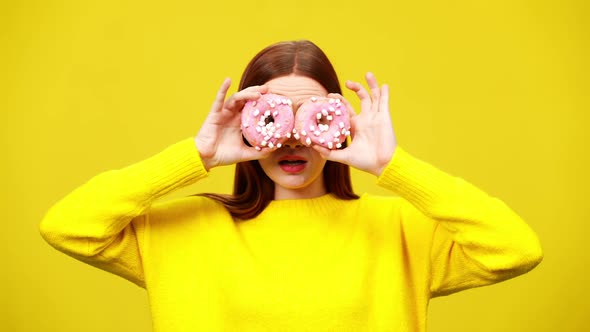 Middle Shot of Charming Joyful Redhead Woman Covering Eyes with Pink Donuts in Slow Motion
