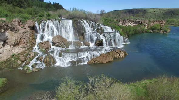 Flying view of waterfall flowing over edge into river