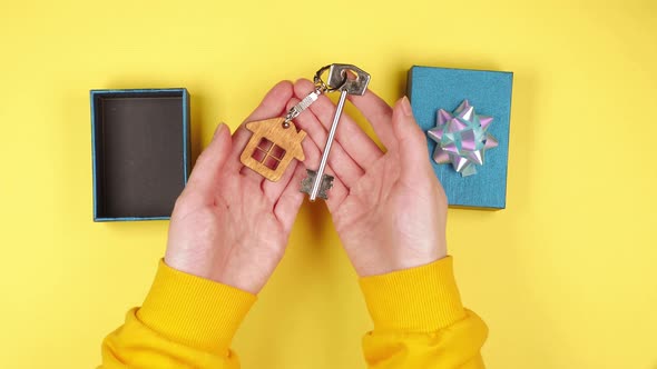 Hands of a young woman open a blue gift box with keys to a new property with a keychain