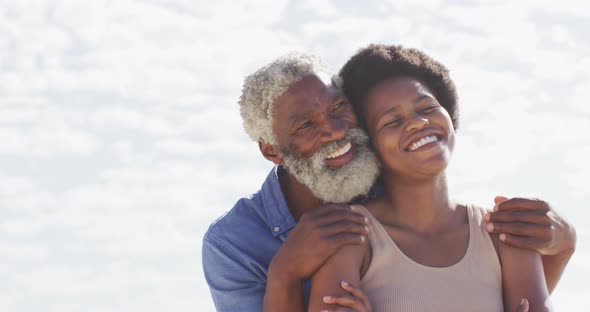 African american couple embracing and looking away on sunny beach