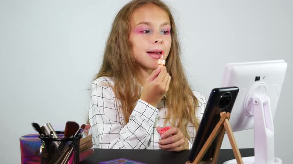 A Girl With Bright Makeup Applies Lip Gloss Looking Into the Smartphone Camera