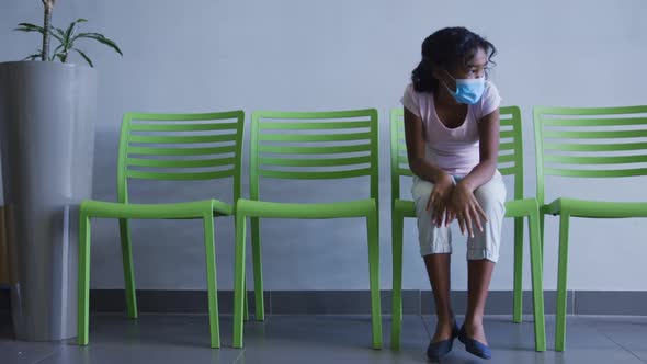 African american girl wearing face mask sitting on a chair at hospital