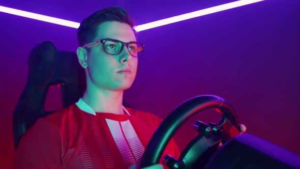 Focused Gamer Playing a Racing Simulator Machine Multicolor Neon Light