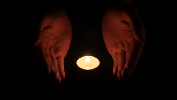 Hands Holding a Burning Candle in Dark