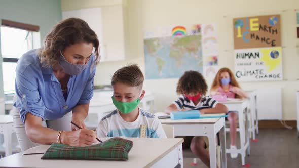 Female teacher wearing face mask teaching a boy in class at school