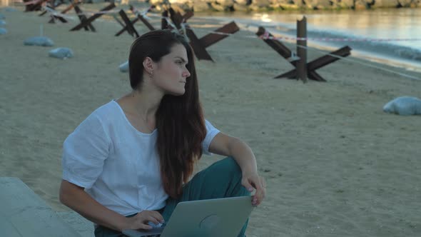 Young Woman With A Laptop Against The Background Of Anti-Tank Hedgehogs In Ukraine