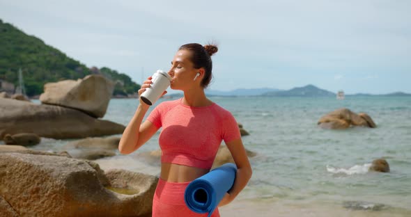 Young Brunette Woman Drinks Water From White Thermo Cup She Stands with Blue Yoga Mat Outdoors on