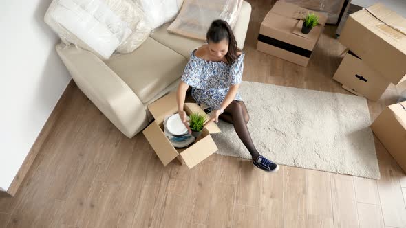 Top View Woman Unpacking Plates and Plants From Cardboard Boxes