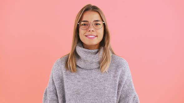 Young Female in Sweater and Glasses is Looking at you and Smiling While Posing Against Pink