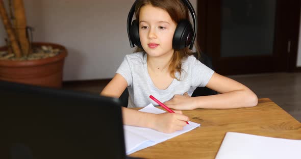 Cute little girl with headphones using laptop to study at home