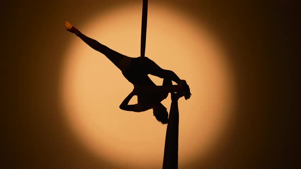 Silhouette of a Young Woman Spins Hanging Upside Down and Twine on Airy Silk