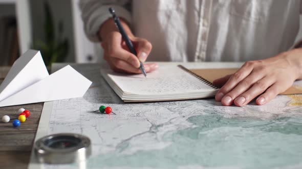 A Tourist Takes Notes In A Diary On The Background Of A Map Of A Laid Route, Planning A Trip