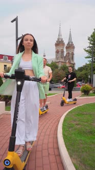 Fashionable charming group of friends riding public rental electric scooters