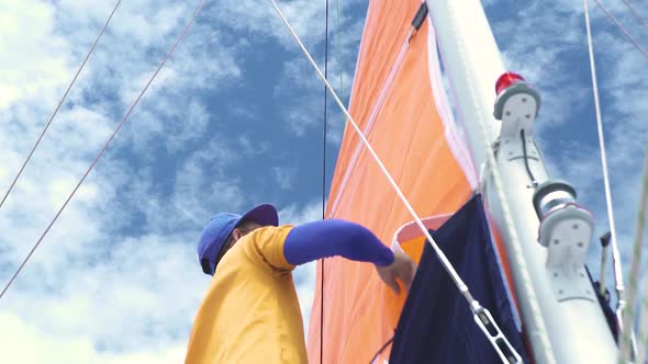 Man Pulling Down Boat's Mainsail in the Background of White Clouds and Blue Sky.