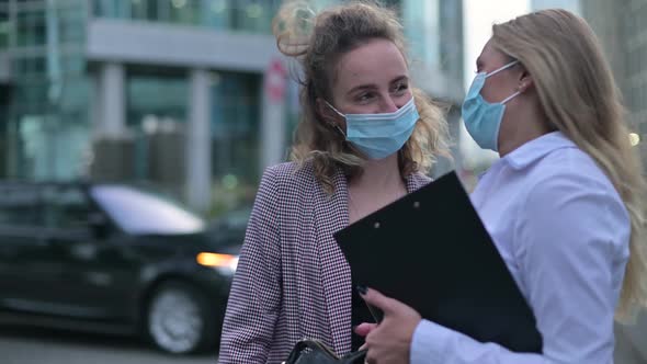 Woman in medical mask talking to colleague on the street after working day