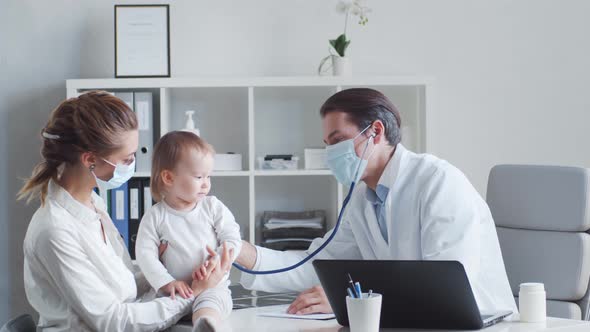 Male pediatrician is examining little baby. Doctor, mother and daughter in medical office.